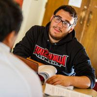 A student sitting at a table having a discussion with a classmate.