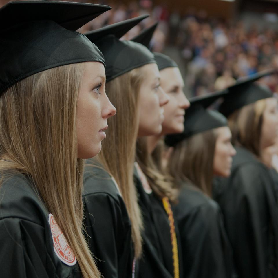 students in cap and gown standing at graduation ceremony.